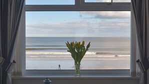 Ein Fenster mit Blick auf den Strand, eine Vase mit Blumen und ein kleines Fenster darüber.