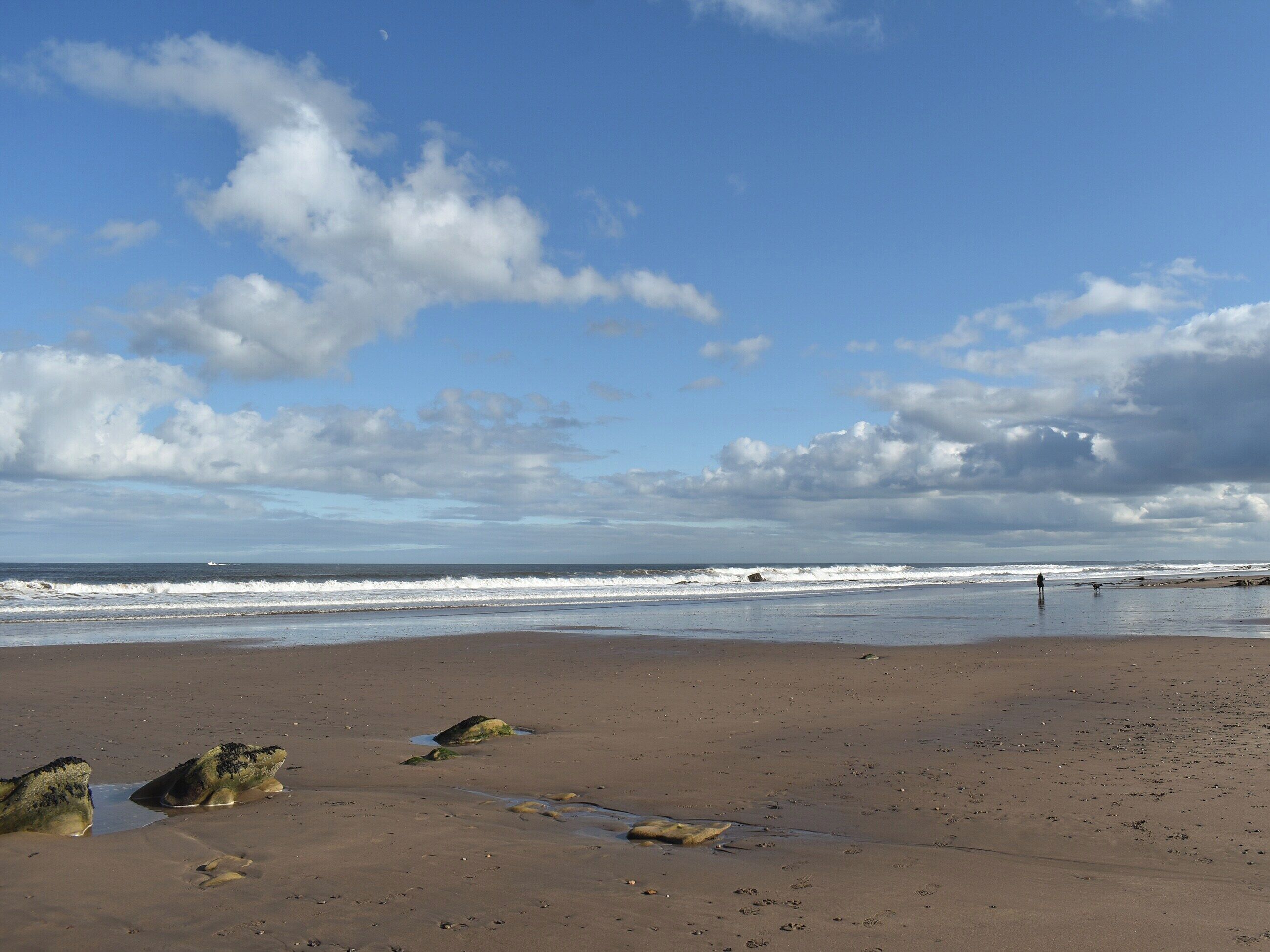 A beach with waves, rocks, and a partly cloudy sky.
