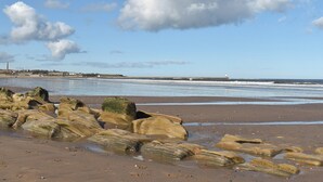 Ein Strand mit großen Felsen im Vordergrund und einem Leuchtturm in der Ferne.
