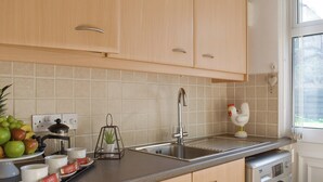 Eine Küche mit hellen Holzschränken, einer Edelstahl-Spüle, einer Waschmaschine und einem Fenster mit Jalousien.