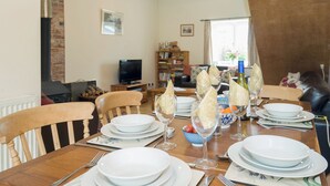 A dining area with a wooden table set for a meal, a television in the background, and a brick wall.