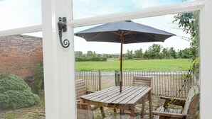 A patio with wooden furniture and a large umbrella, overlooking a grassy area and a brick wall.