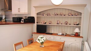 A kitchen with white cabinets, a microwave, a television, and a shelf with decorative plates.