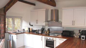 Una cocina con armarios blancos, electrodomésticos de acero inoxidable, vigas de madera y un ventanal con rejas.
