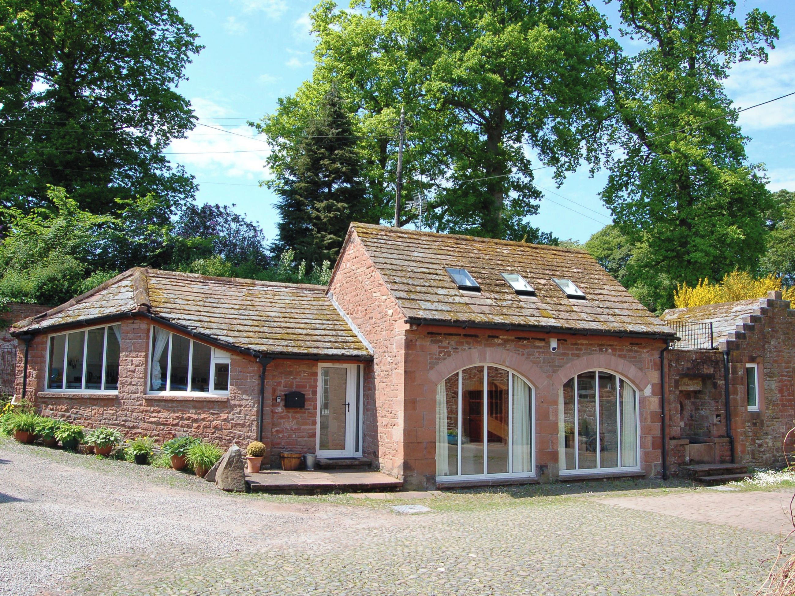 A two-story brick building with a sloped roof, large windows, and a gravel driveway.