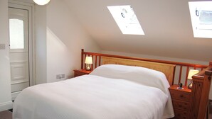A bedroom with a large bed, wooden headboard, two bedside tables with lamps, and skylights.