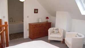 A bedroom with a bed, a wooden dresser, a chair, and a view of a bathroom with a bathtub.
