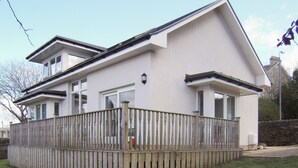 A two-story house with a wooden deck and a stone wall in the background. - 3 bedroom accommodation in Rothesay, Isle of Bute (Rothesay, Isle of Bute)
