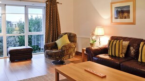 A living room with a sofa, armchair, ottoman, coffee table, and a lamp. - 3 bedroom accommodation in Rothesay, Isle of Bute (Rothesay, Isle of Bute)