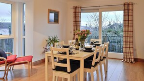 A dining area with a table set for four, a potted plant, and a view of the outdoors through large windows. - 3 bedroom accommodation in Rothesay, Isle of Bute (Rothesay, Isle of Bute)