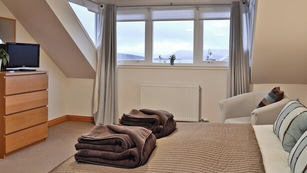 A bedroom with a bed, a TV on a dresser, a radiator, and a view of the outdoors. - 3 bedroom accommodation in Rothesay, Isle of Bute (Rothesay, Isle of Bute)