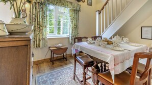 Une salle à manger avec une table mise pour le thé, un buffet en bois et une fenêtre avec des rideaux.
