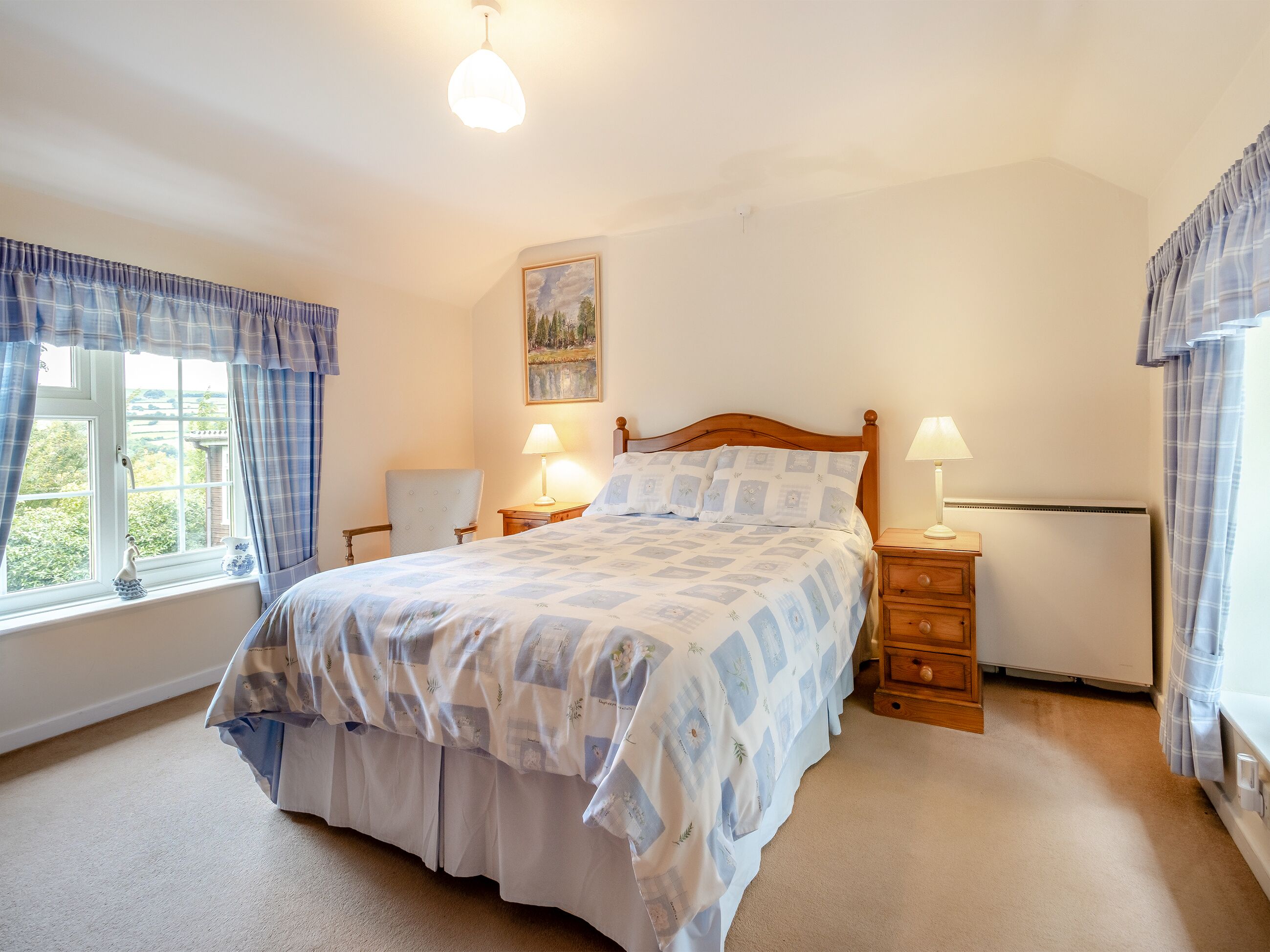 A bedroom with a bed, two bedside tables, a window with curtains, a painting on the wall, and a radiator.