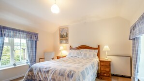 Une chambre à coucher avec un lit, deux tables de chevet, une fenêtre avec des rideaux, un tableau au mur et un radiateur.