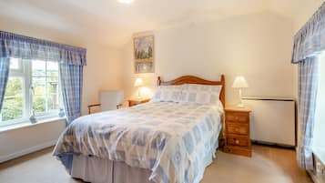 A bedroom with a bed, two bedside tables, a window with curtains, a painting on the wall, and a radiator.