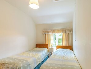 Une chambre avec deux lits, une fenêtre avec des rideaux, une table de chevet avec une lampe et un luminaire au plafond.