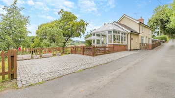 A house with a conservatory, a paved driveway, and a wooden fence.
