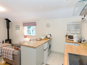 A compact kitchen with a wood-burning stove, a washing machine, a microwave, and a small dining area.