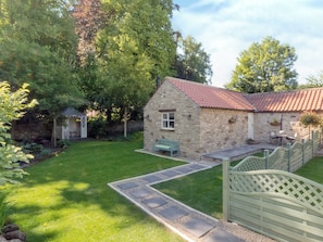 A stone cottage with a red-tiled roof, a small garden, and a wooden gate.