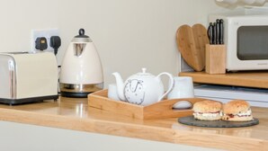 A kitchen with a toaster, kettle, teapot, mug, wooden cutting board, sandwich, and a microwave.