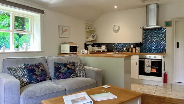 A living room with a sofa, a coffee table, a kitchen with a microwave, oven, and a tiled backsplash.