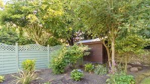 A garden with a wooden shed, a stone wall, and a wooden fence.