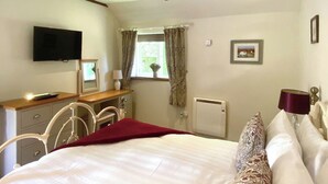 A bedroom with a bed, a desk with a chair, a television, a window with curtains, a radiator, and a framed picture on the wall.