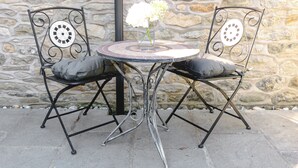 A stone wall, two metal chairs with cushions, and a small round table with a vase of flowers.
