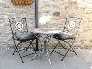 Eine Steinsäule, zwei Metallstühle mit Kissen und ein runder Tisch mit einem Blumenstrauß.