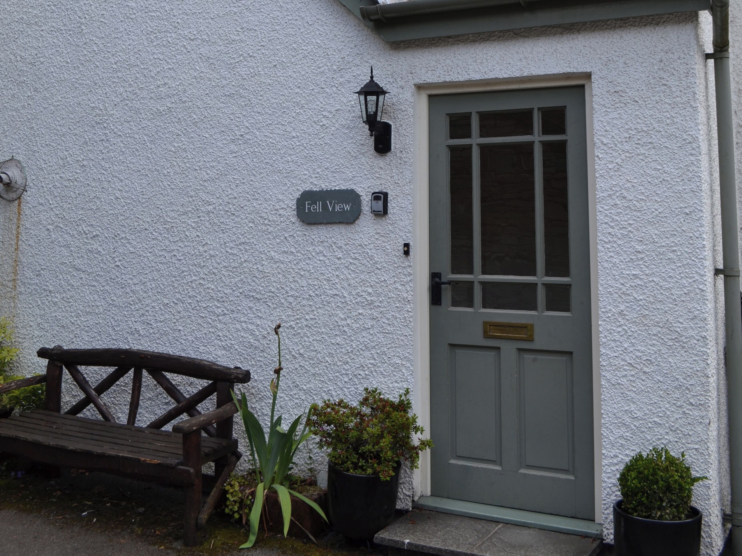 A white building with a grey door, a bench, and potted plants.