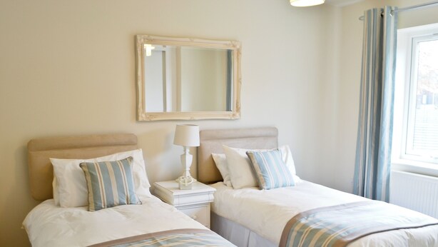 Une chambre d’hôtel avec deux lits, une table de chevet avec une lampe, un miroir au mur et une fenêtre avec des rideaux.