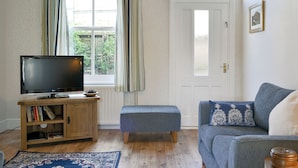 Un salon avec un téléviseur posé sur un meuble en bois, un canapé bleu, un pouf assorti et un tapis à motifs.