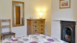 Une chambre à coucher avec un lit, une commode en bois, une chaise, un miroir, une lampe et une cheminée.