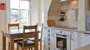 Une cuisine équipée d’une table à manger, de chaises, d’un four encastré et d’une fenêtre agrémentée d’un lambrequin à motifs.