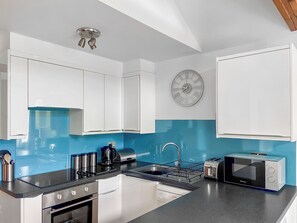 Eine moderne Küche mit weißen Schränken, einer blauen Spritzschutzwand, einem Geschirrspüler von Bosch, einer Mikrowelle und einem Spülbecken.