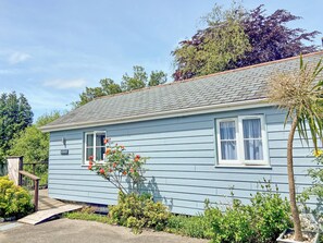 Et lyseblåt hus med skråtag, en lille veranda og en have med forskellige planter og blomster.