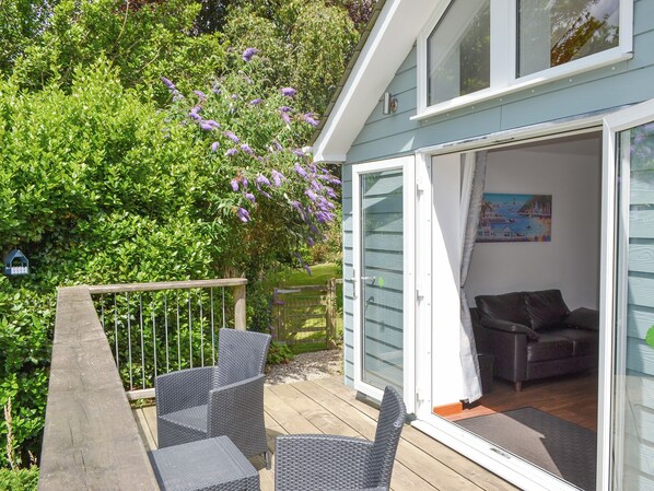 An open sliding glass door leading to a living area with a dark-colored sofa and a wooden deck. - A peaceful haven with a summerhouse and just minutes from Mevagissey and Fowey. (St Austell)