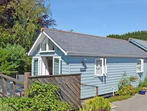 A light blue house with a grey roof, a wooden deck, and a garden with various plants. - A peaceful haven with a summerhouse and just minutes from Mevagissey and Fowey. (St Austell)