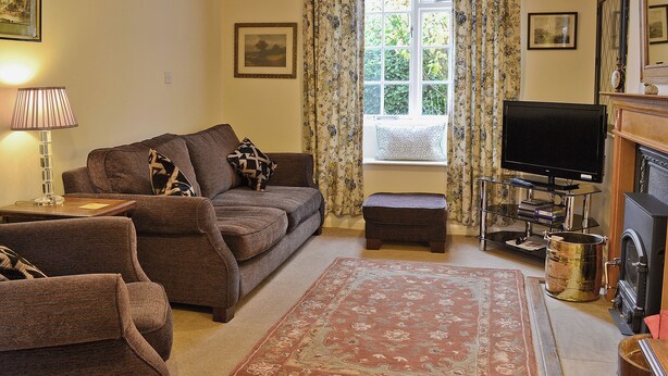 Una sala de estar acogedora con sofá, sillón, reposapiés, televisor de pantalla plana, chimenea y un amplio ventanal con cortinas.