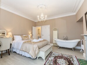 Une chambre à coucher comprenant un lit, une table de chevet, une lampe, un lustre, ainsi qu’une salle de bain avec une baignoire et un lavabo.