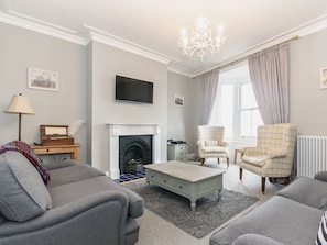 A living room with a fireplace, two armchairs, a coffee table, and a television mounted on the wall.