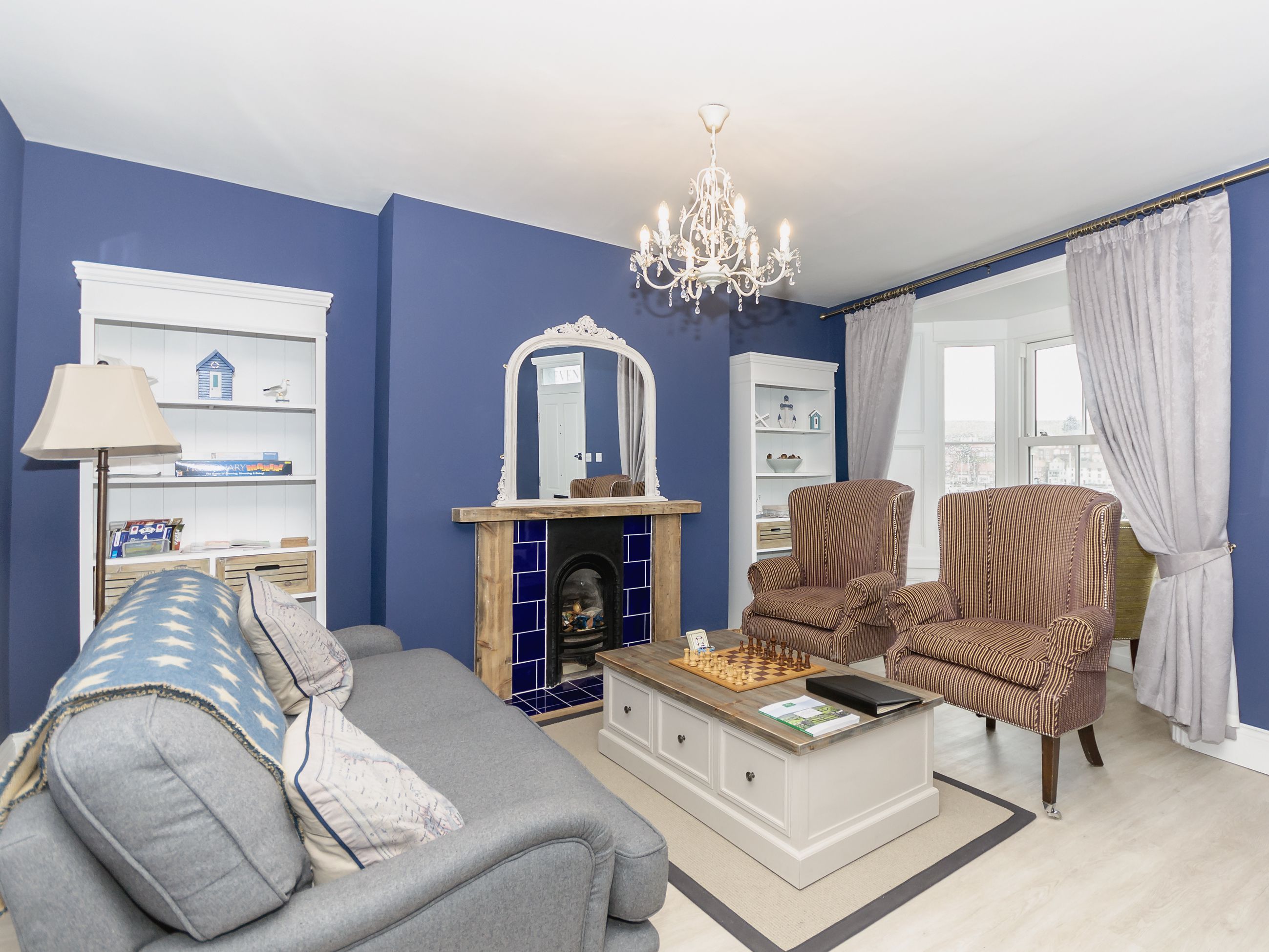 Una sala de estar con sofá, sillón, chimenea, estantería y candelabro.