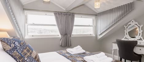 Un dormitorio con una cama grande, un escritorio, una silla, una ventana con cortinas y una lámpara en el techo.