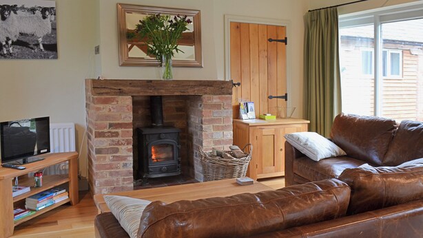 Una sala de estar acogedora con chimenea, sofá de cuero, mesa de centro de madera y televisor sobre un mueble de madera.