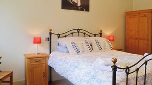 Una cama bien hecha con ropa de cama estampada, una mesita de noche de madera con lámpara y un armario de madera en una habitación con suelo de madera.