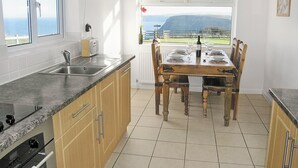 Une cuisine avec un coin repas, une vue sur l’extérieur et une horloge au mur.