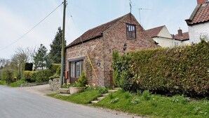 A brick house with a tiled roof, a visible chimney, and a small garden with yellow flowers. - 5 steps to entrance. (Burythorpe near Malton)