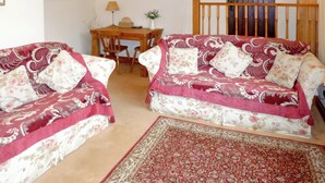 A living room with two patterned sofas, a wooden dining table, chairs, a clock, and a wooden staircase. - 5 steps to entrance. (Burythorpe near Malton)