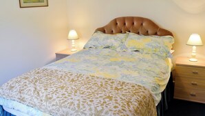 A neatly made bed with floral bedding, two bedside lamps, and a small wooden nightstand with drawers. - Pig Sty Cottage - E1867 (West Milton)