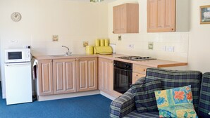 A compact kitchen with wooden cabinets, a microwave, a toaster, and a dishwasher. - Pig Sty Cottage - E1867 (West Milton)